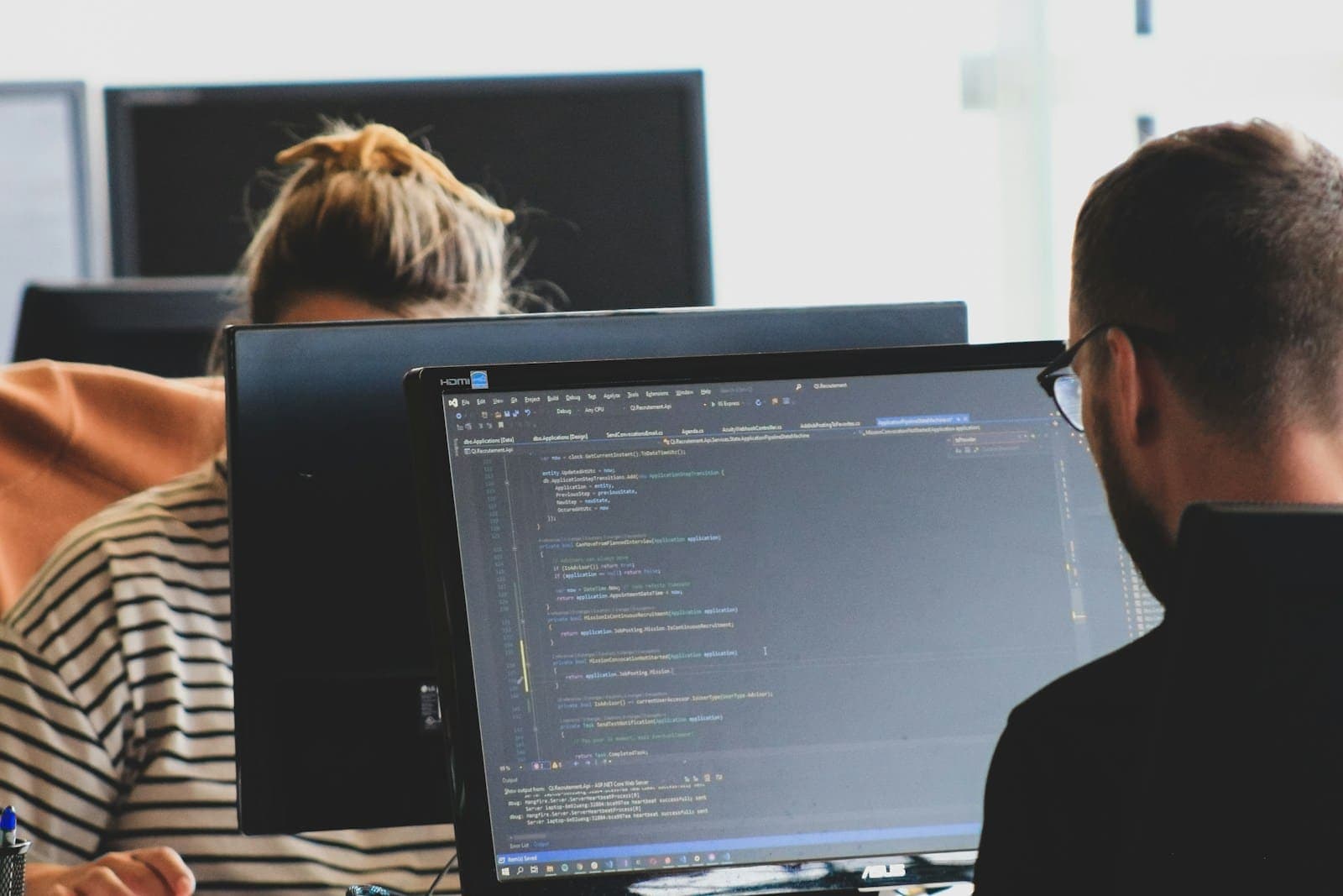 Duas pessoas programando em monitores em um escritório claro
